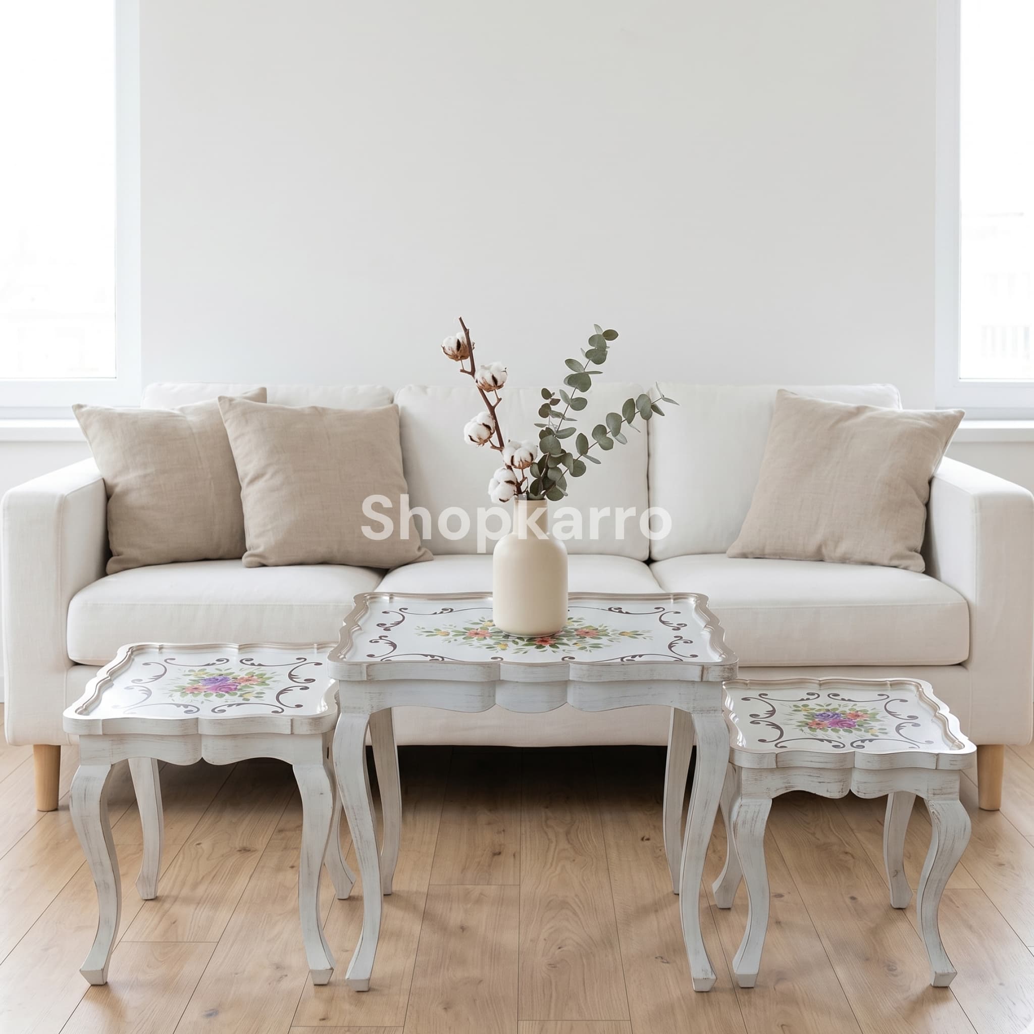 Set of three white floral nesting tables stacked beside cream sofa in bright elegant living room